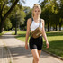 A woman in a white crop top and black shorts walks in a park, wearing a brown bum bag with a logo.