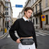 A black fanny pack worn around the waist, with a logo, against an urban street backdrop.