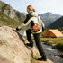 A drink bottle holder waist bag in orange is worn by a person climbing a rocky surface near a campsite.