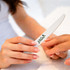 A wooden knife-shaped nail file with a white surface, held between two hands. It has a green logo.
