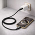 A black braided charging cable connected to a phone and a wall charger. The phone displays a battery charge percentage.