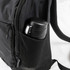 A black daypack features a side mesh pocket holding a black drink bottle. The bag has zippers and adjustable straps.