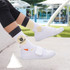 Custom patterned woven socks in white with yellow and grey designs, worn with white footwear. Features a logo.
