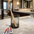 A large flat handle toothbrush with a pink bristle head in a glass, beside two tubes of toothpaste on a bathroom countertop.