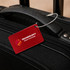 A red rectangular luggage tag attached to a black suitcase handle, featuring a logo.