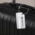 A square aluminium luggage tag in silver attached to a black suitcase, featuring a logo and a name label.