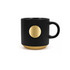 A ceramic coffee mug in black with a bronze medal accent and ribbed texture. Features a handle and a logo.