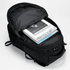 A black Fitzroy Backpack open, revealing stacked magazines and a notebook inside. The bag has a sleek design and features.