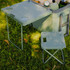 A green cooler box with a table and a small folding chair, placed on grass, featuring drink holders.