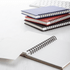 A stack of spiral-bound notebooks in blue, red, black, and white, with one opened to reveal lined pages.