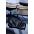 A black bag hanger clips onto a desk, supporting a black clutch. A computer keyboard and remote are in the background.
