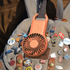 A peach pocket fan attached to a backpack, surrounded by various decorative pins and badges.