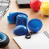 A blue keyring featuring a compact, rolled-up poncho and a snap closure, surrounded by colourful items on a table.