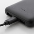 A black power bank with USB ports and a charging cable connected, made from recycled ABS material.