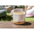 A wireless speaker with a silver top and a natural wood base, placed on a wooden surface in a grassy outdoor setting.