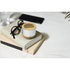 A compact white and wood wireless speaker sits on a stack of books, alongside glasses and a smartphone.