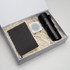 A black drink bottle, notebook, white speaker, and pen in a gift box with shredded paper filling.