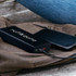 A black power bank with a logo connected to a smartphone, resting on a brown bag.