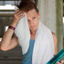 A person with short hair is drying their forehead with a white towel, holding a blue drink bottle in their hand.