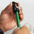 A black and grey pencil sharpener being used on a green carpenter’s pencil, surrounded by wood shavings.