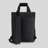 A black tote pack with adjustable straps and a structured design, featuring a front zip pocket and a top handle.