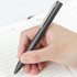 A metal pen in dark grey, held in a hand over an open notebook with lined pages.