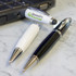 A collection of metal pens including a white pen and a black pen, featuring a logo on one, placed beside a laptop.