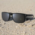 A pair of black sunglasses resting on sandy ground, featuring a simple design and grey lenses.