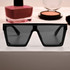 Black oversized sunglasses with dark lenses, displayed in front of cosmetics on a flat surface.