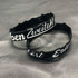 Two black silicone wristbands featuring white custom designs, displayed on a grey background.
