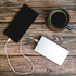 A white and a black power bank with a charging cable, placed beside a cup of coffee on a wooden surface.
