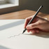 A hand holding a grey pencil, drawing a wavy line on a white sheet of paper, with natural light coming through a window.