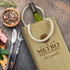 A jute double wine carrier in beige, with a bottle inside, accompanied by utensils and a bowl of mixed peppercorns.