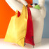 A yellow and red foldaway shopper tote bag, featuring a drawstring closure and a logo, displayed on a mannequin.