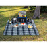 A picnic rug in shades of blue and grey, laid out with plates, glasses, cutlery, and a picnic basket on grass.