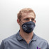 A grey face mask with a logo, worn by a person, featuring ear loops for a secure fit.