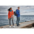 A woman in an orange softshell jacket and a man in a blue softshell jacket stand by the water, featuring a backpack.