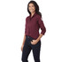 A women's long sleeve button-up shirt in burgundy, featuring a logo on the sleeve and styled with dark jeans.