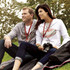 A grey and white zip-up hoodie worn by a woman and a man, both sitting outdoors with a camera. They have lanyards.