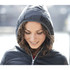 A woman wearing a navy insulated jacket with a hood, smiling gently in an outdoor setting.