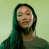 A model with long hair wears wireless earbuds against a green background. The design features a sleek, modern style.