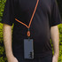 A phone lanyard with an orange cord is worn around the neck, holding a black smartphone.