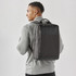 A man wearing a grey sweater carries a dark grey laptop backpack on his back, featuring a simple logo.