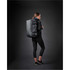 A woman wearing black activewear carries a grey Equinox 30 Duffel Bag on her back against a dark background.