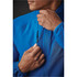 A close-up of a man fastening a blue quilted jacket with a zip, featuring a sleek collar and a logo.