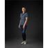 A woman wearing a navy and white striped polo shirt, paired with blue jeans and white shoes, standing against a dark background.