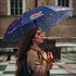 A full-colour umbrella in dark tones with a vibrant pattern, held by a woman with long hair, featuring a logo.