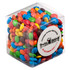 A clear cube filled with colourful chocolate-coated candy, including red, blue, yellow, green, and brown M&Ms.