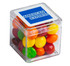 A transparent cube containing colourful Skittles in various shades, with a branding logo on the lid.