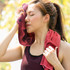 A woman wipes her forehead with a red cooling towel, showcasing its texture and functionality in an outdoor setting.